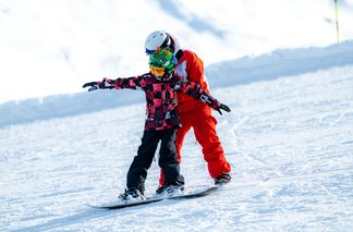 Snowboarder Kind lernt snowboarden mit Hilfestellung 