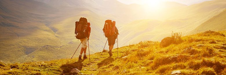 2 Wanderer gehen mit Rucksack, Wanderstöcken und Bergschuhe im Sonnenuntergang